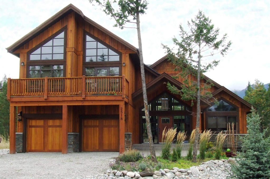 A large timber-frame home with tall windows, a balcony and a double garage with wood doors