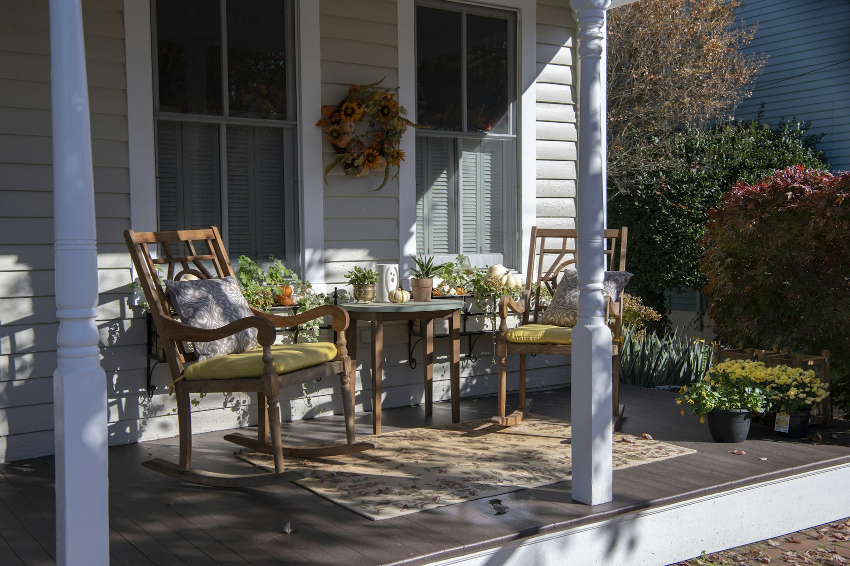 A porch with two wooden rocking chairs, a small table and an autumn wreath