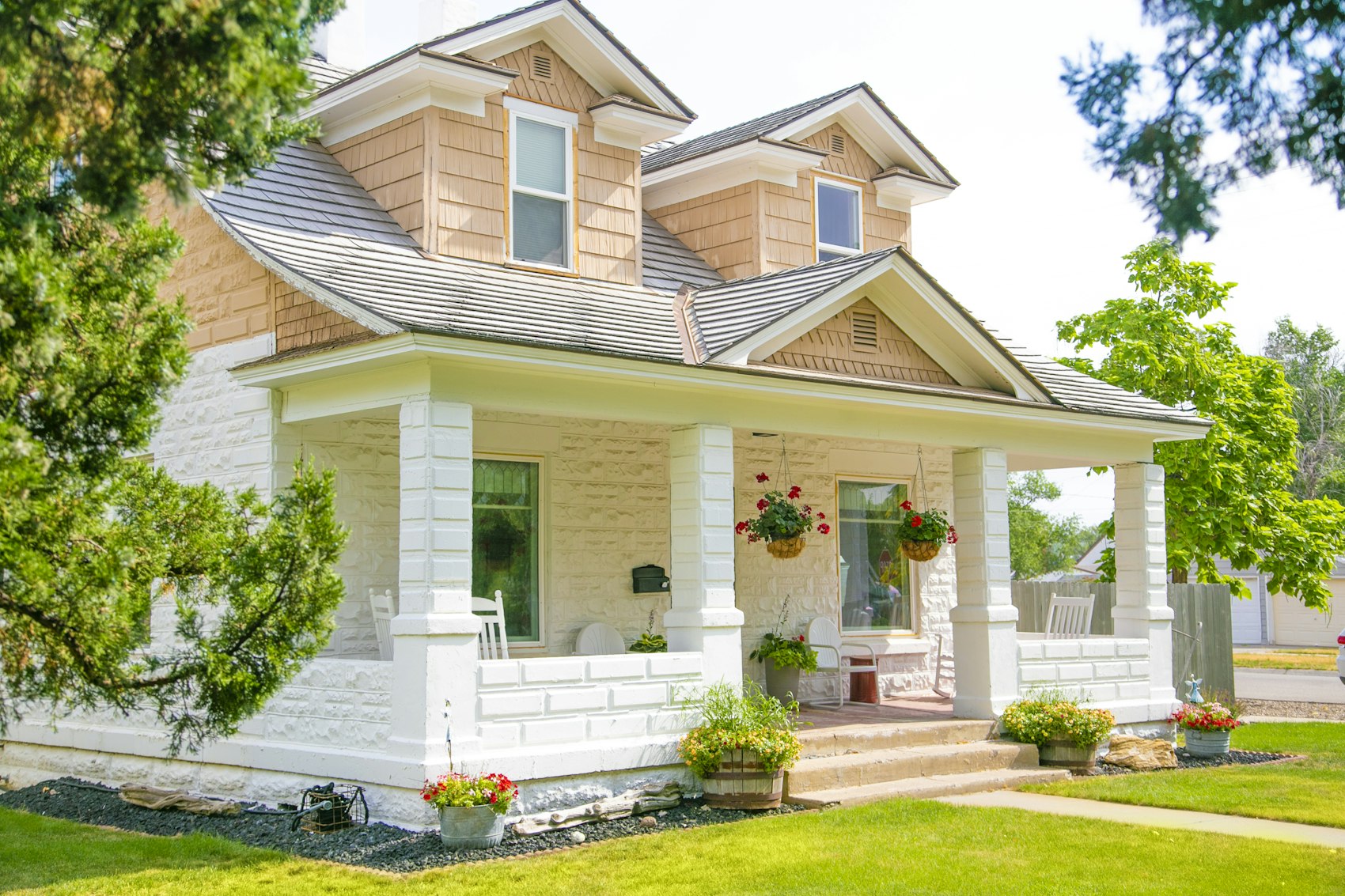 A white house with a covered front porch, hanging flower baskets and a green lawn